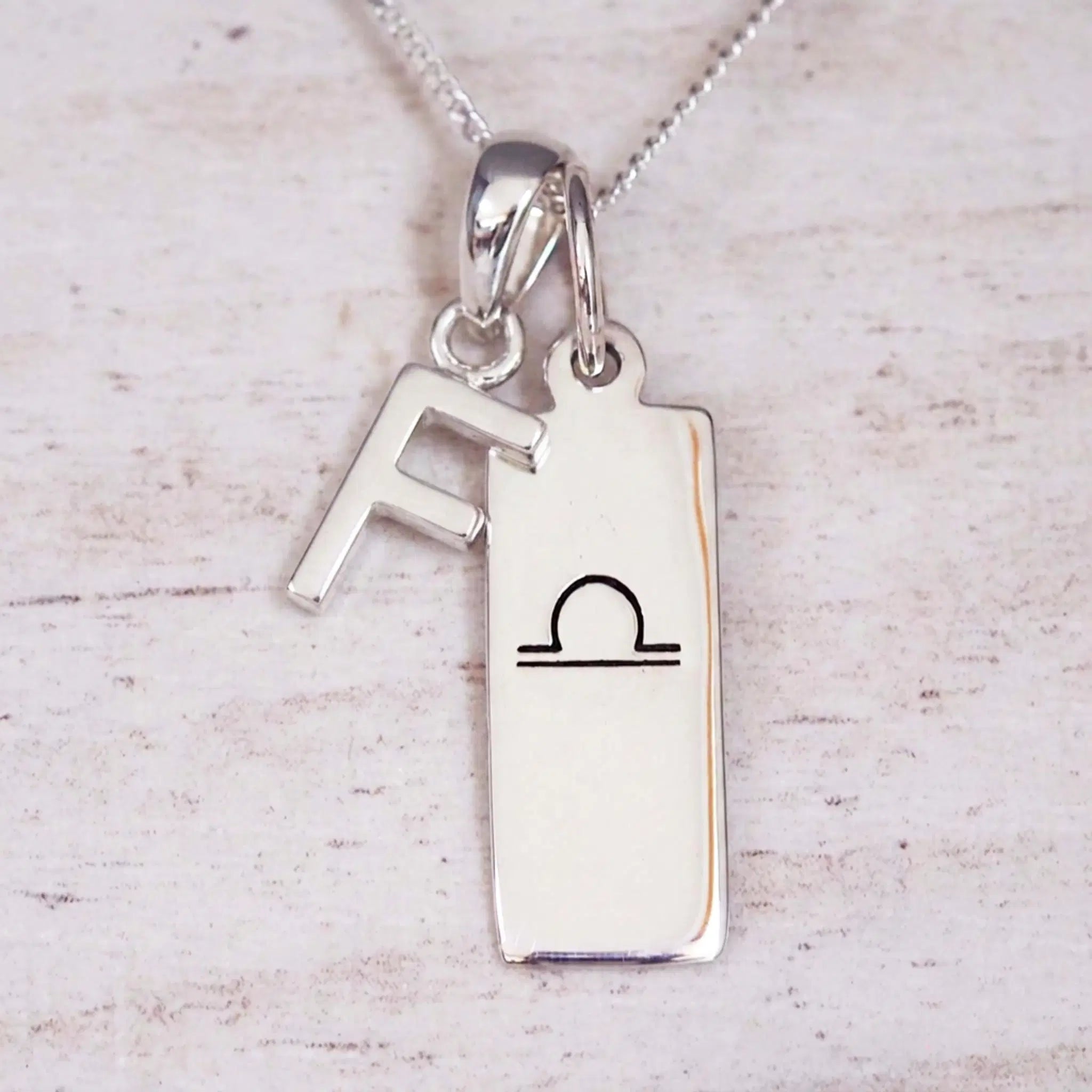 sterling silver initial f libra zodiac star sign pendant necklace against a light wooden background