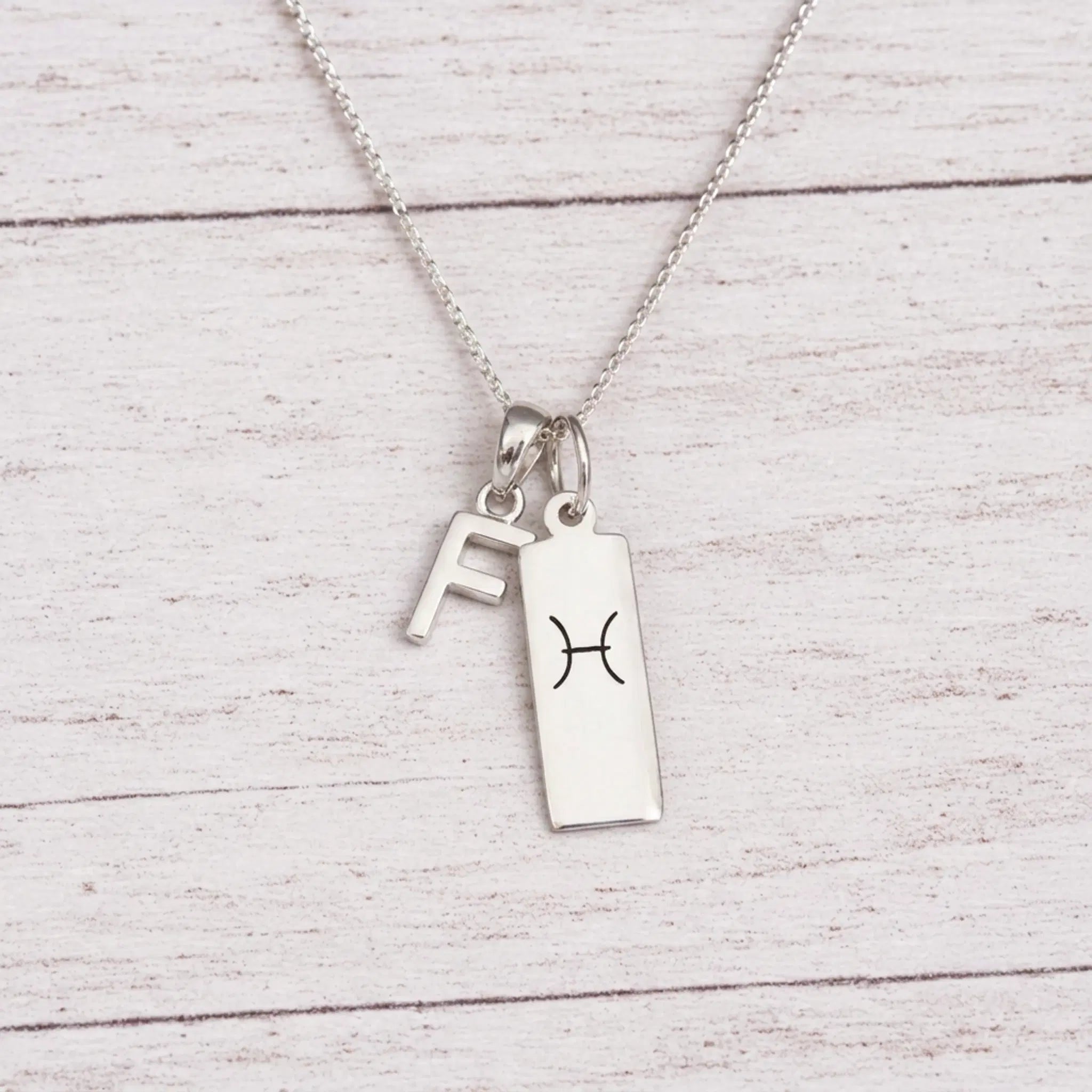 sterling silver F initial Pisces Necklace on a fine silver chain against a light wooden background