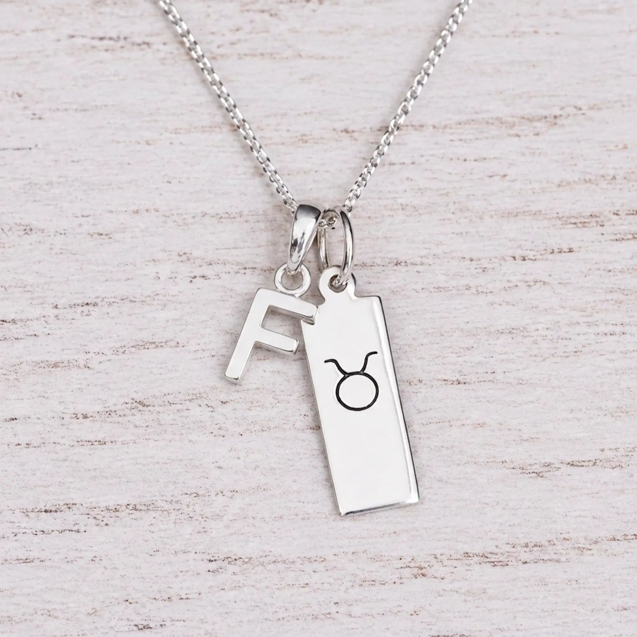 Sterling silver F initial Pendant and Taurus Necklace on a fine silver chain on a light wooden background