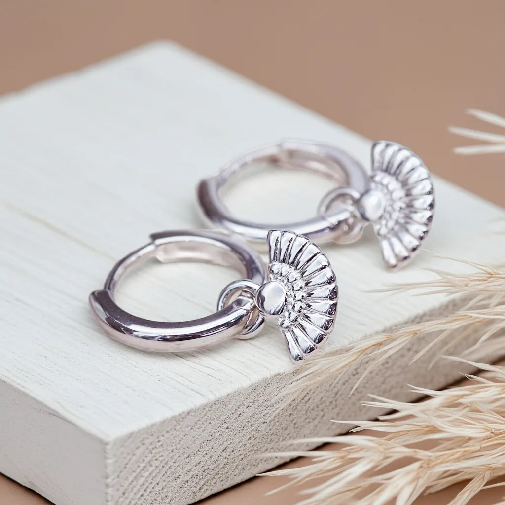 Pair of silver hoop earrings with angel wing designs on a textured surface.