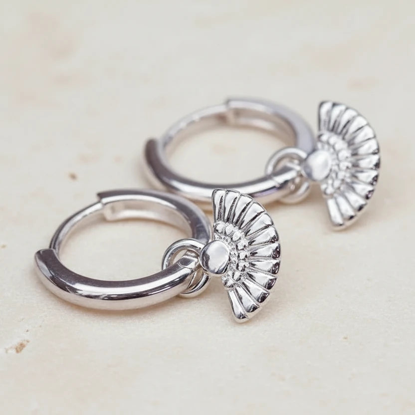 Pair of silver hoop earrings with angel wing designs on a textured surface.