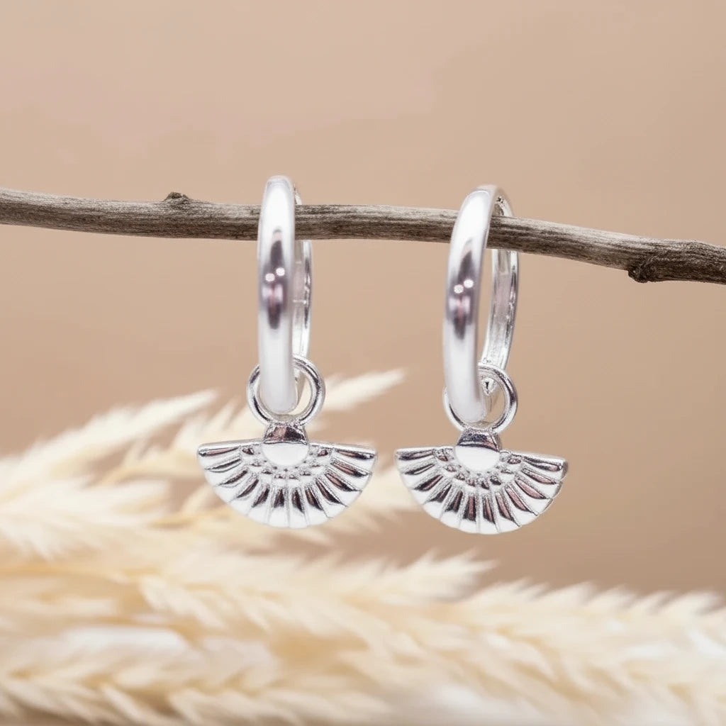 Silver hoop earrings with a textured design on a wooden surface with dried grass.