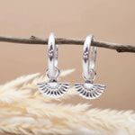Silver hoop earrings with a textured design on a wooden surface with dried grass.
