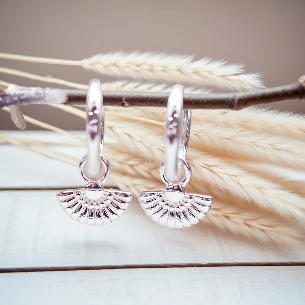 Silver hoop earrings with fan-shaped charms on a branch with dried grass.