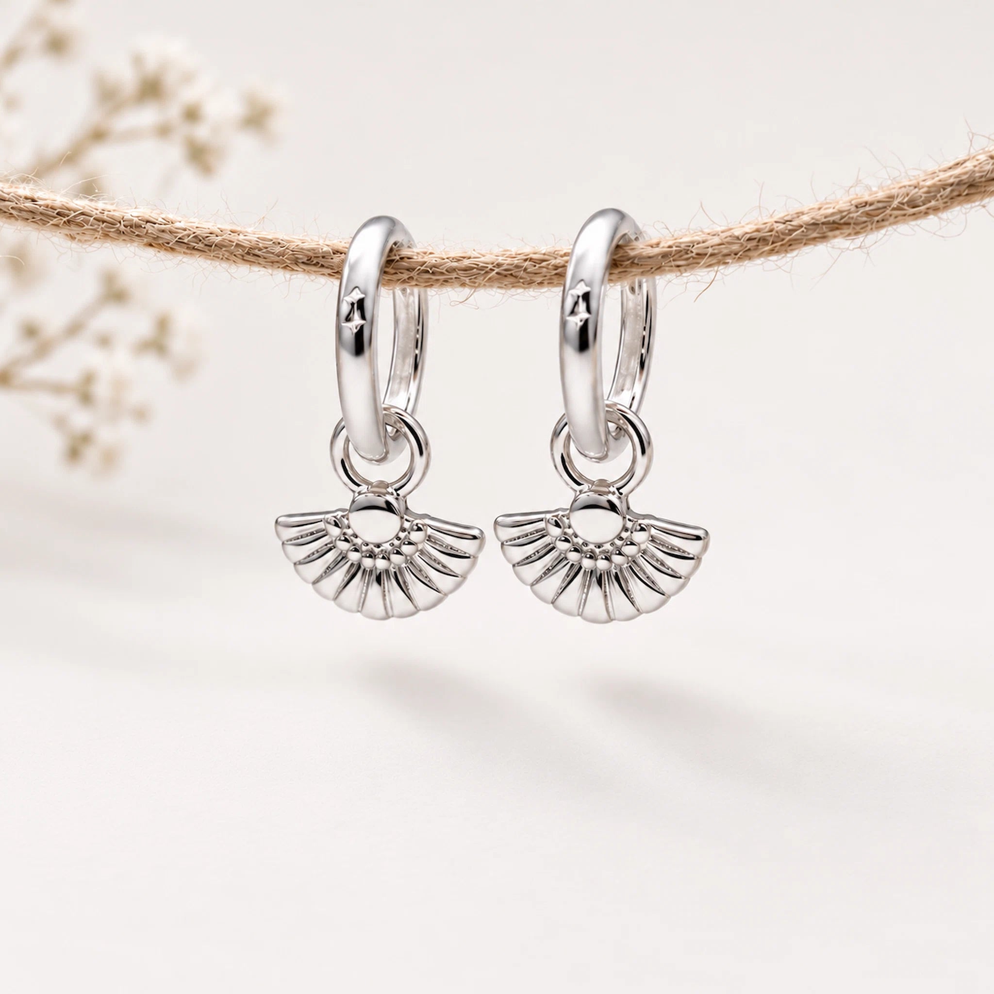 Silver hoop earrings with fan-shaped charms on a natural background