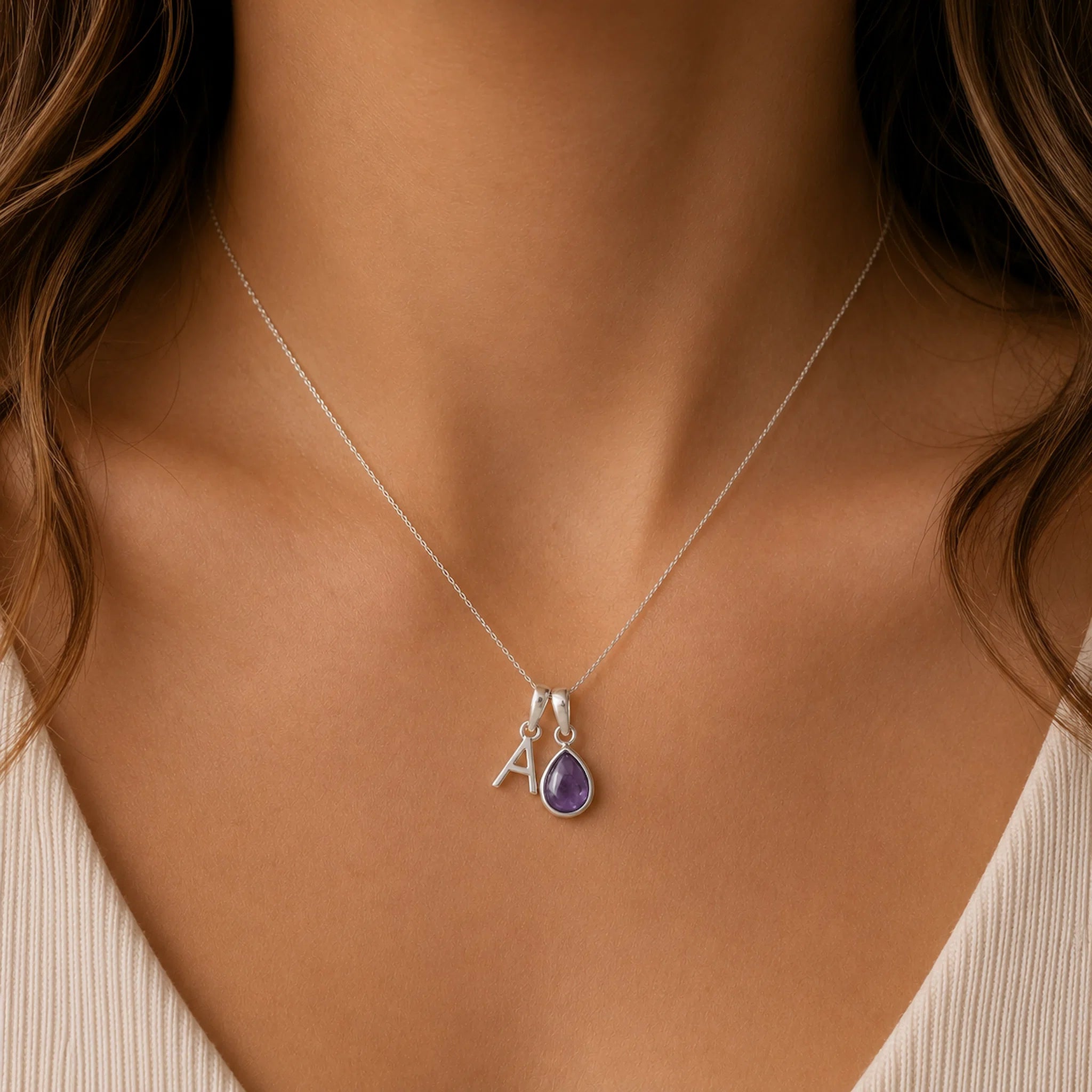 close up of a Silver necklace worn on a woman, with a teardrop-shaped february birthstone amethyst gemstone pendant and a silver 'A' charm