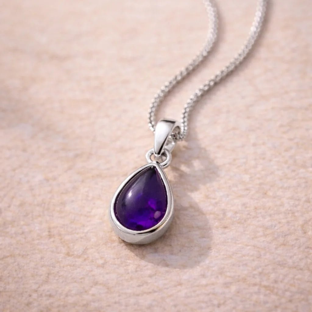 Sterling Silver necklace with a purple teardrop natural amethyst gemstone pendant on a beige background