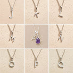 Collection of silver necklaces with initial pendant J to Q on a beige background as personalised letter options to add to a February Birthstone Amethyst Necklace.