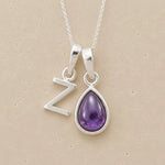 Silver necklace with a teardrop-shaped february birthstone amethyst gemstone pendant and a silver 'Z' charm on a beige background.