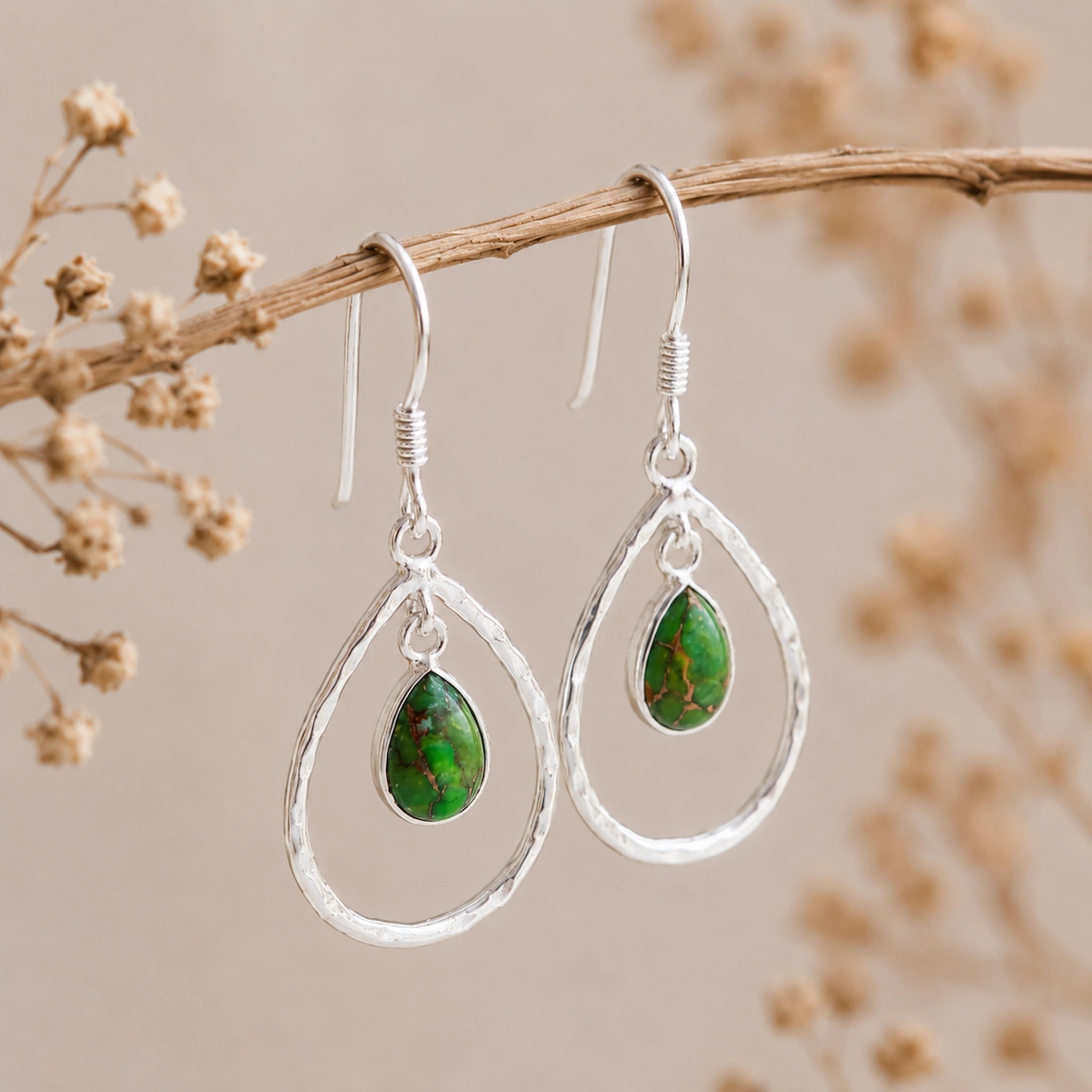 Silver french hook teardrop earrings with green turquoise stones on a branch with dried flowers.