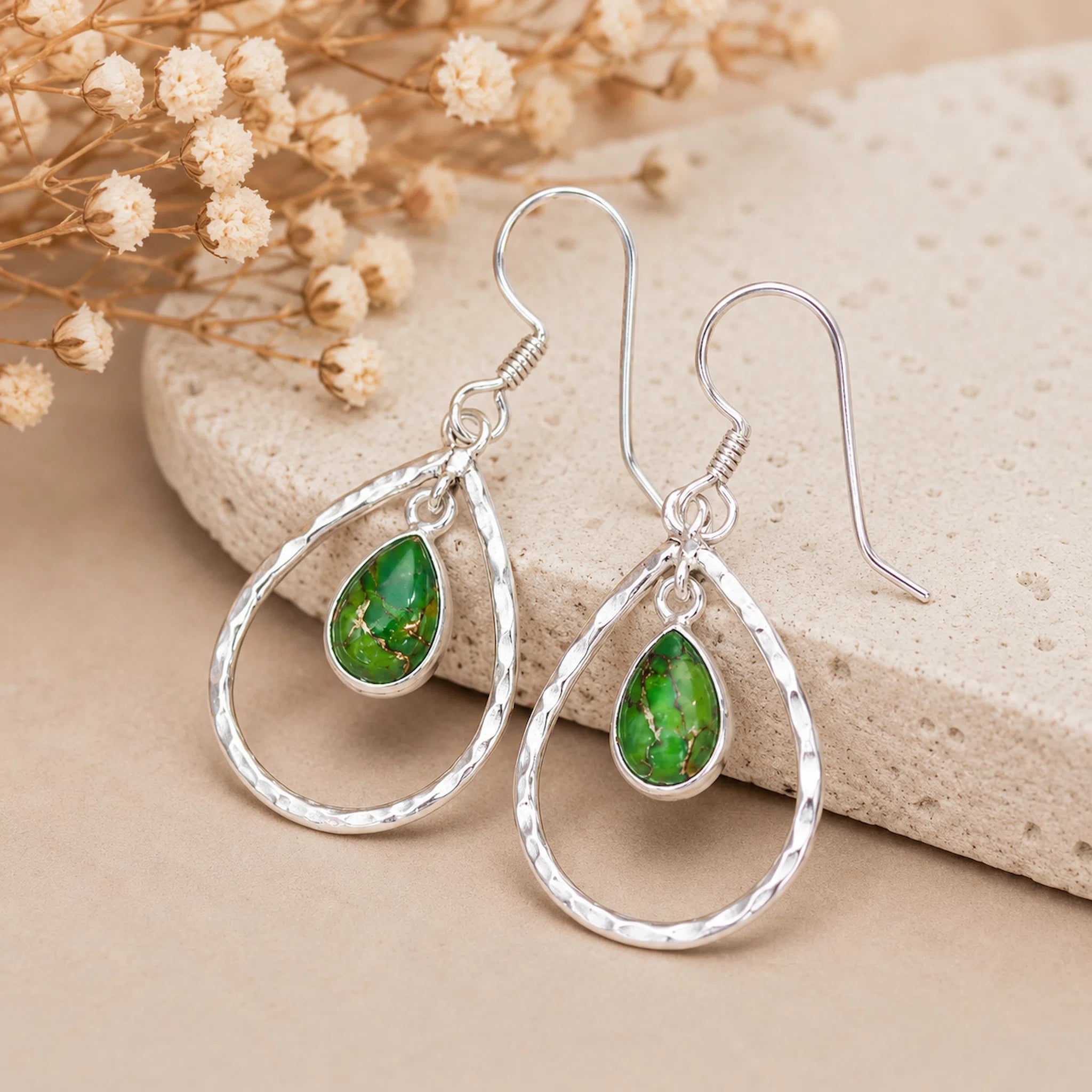 pair of sterling silver french hook earrings with teardrop natural green turquoise stones resting on a stone