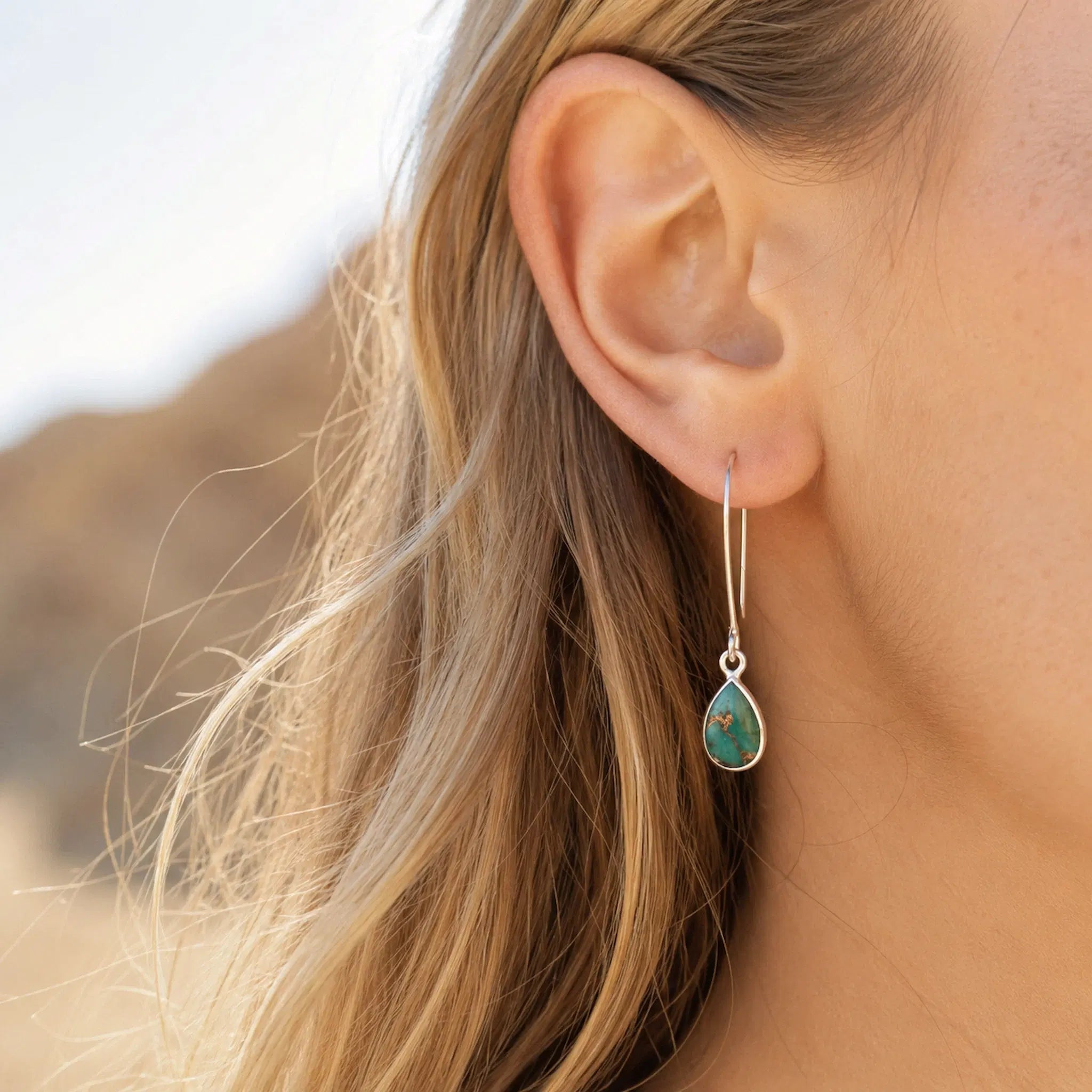 woman wearing a sterling silver long hook earring with a teardrop natural turquoise gemstone