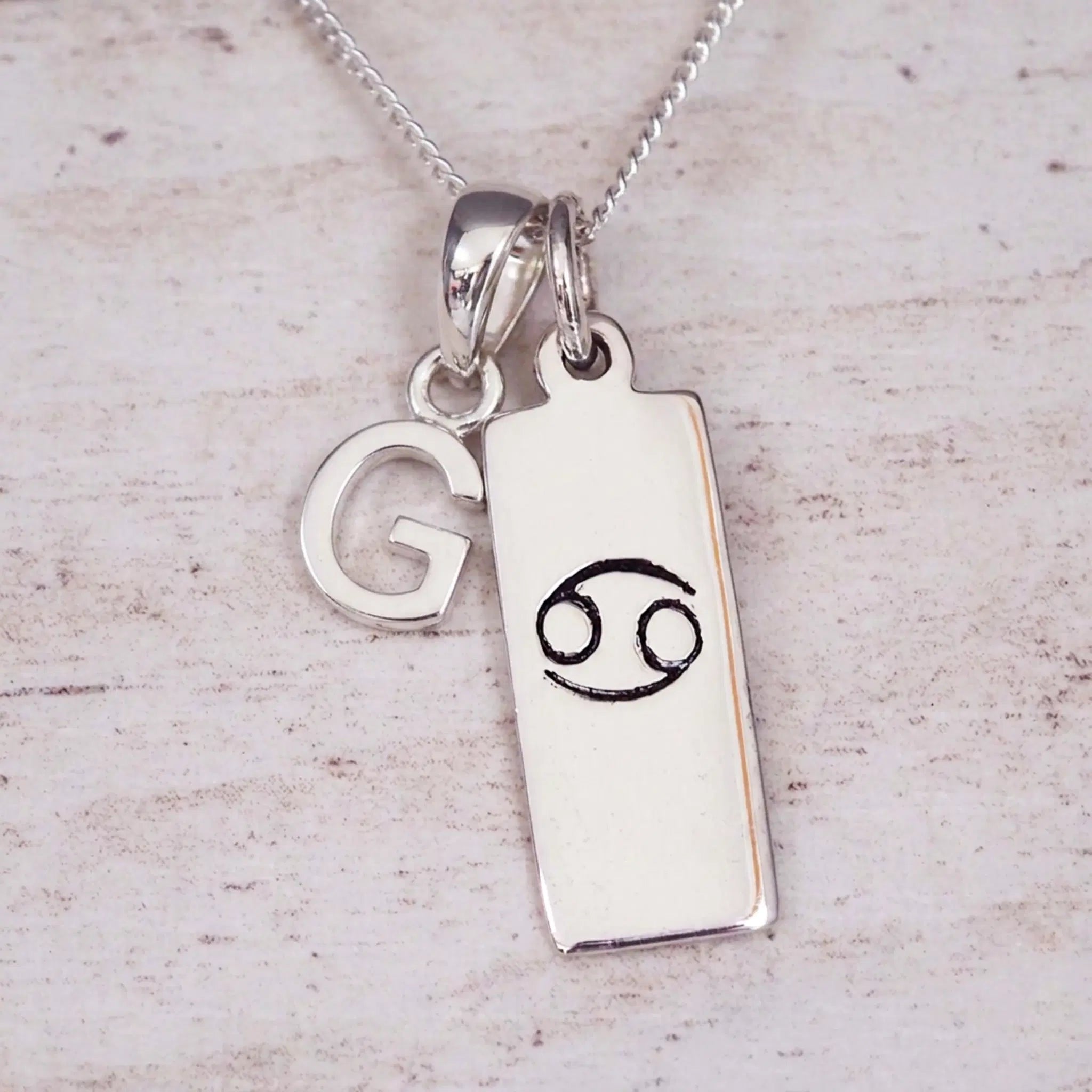 Sterling Silver G Initial Cancer Zodiac Star Sign Necklace on a fine silver chain against a light wooden background