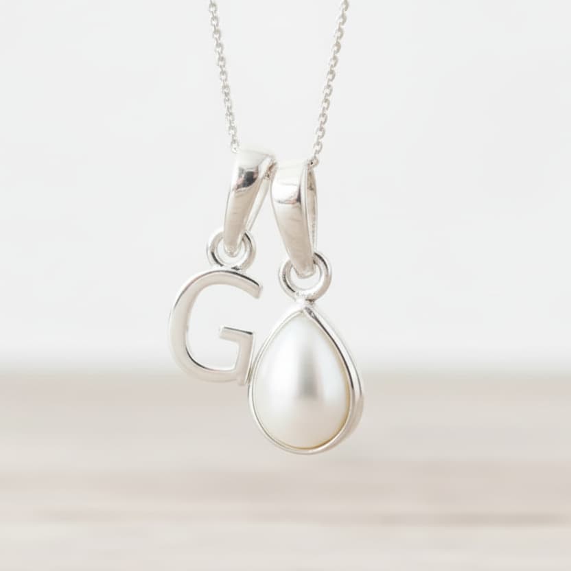 Silver necklace with a teardrop-shaped natural pearl pendant and a ‘G’ initial pendant on a white background