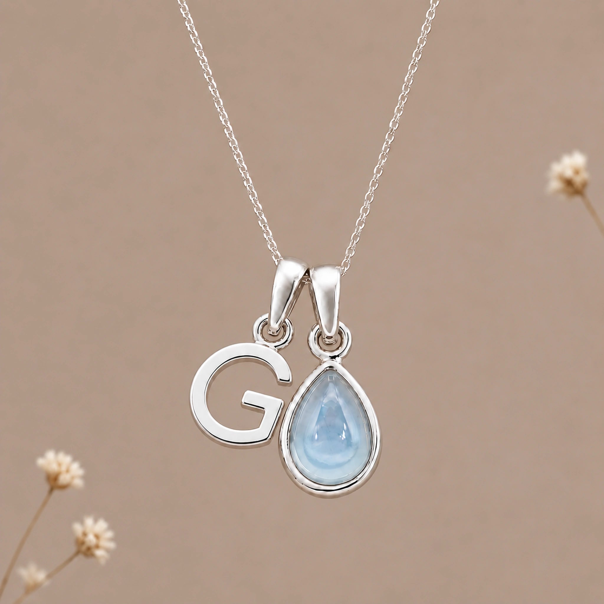 Sterling silver initial G and November natural blue topaz necklace on a taupe background with sparse ivory flowers