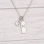 sterling silver G initial Pisces Necklace on a fine silver chain against a light wooden background