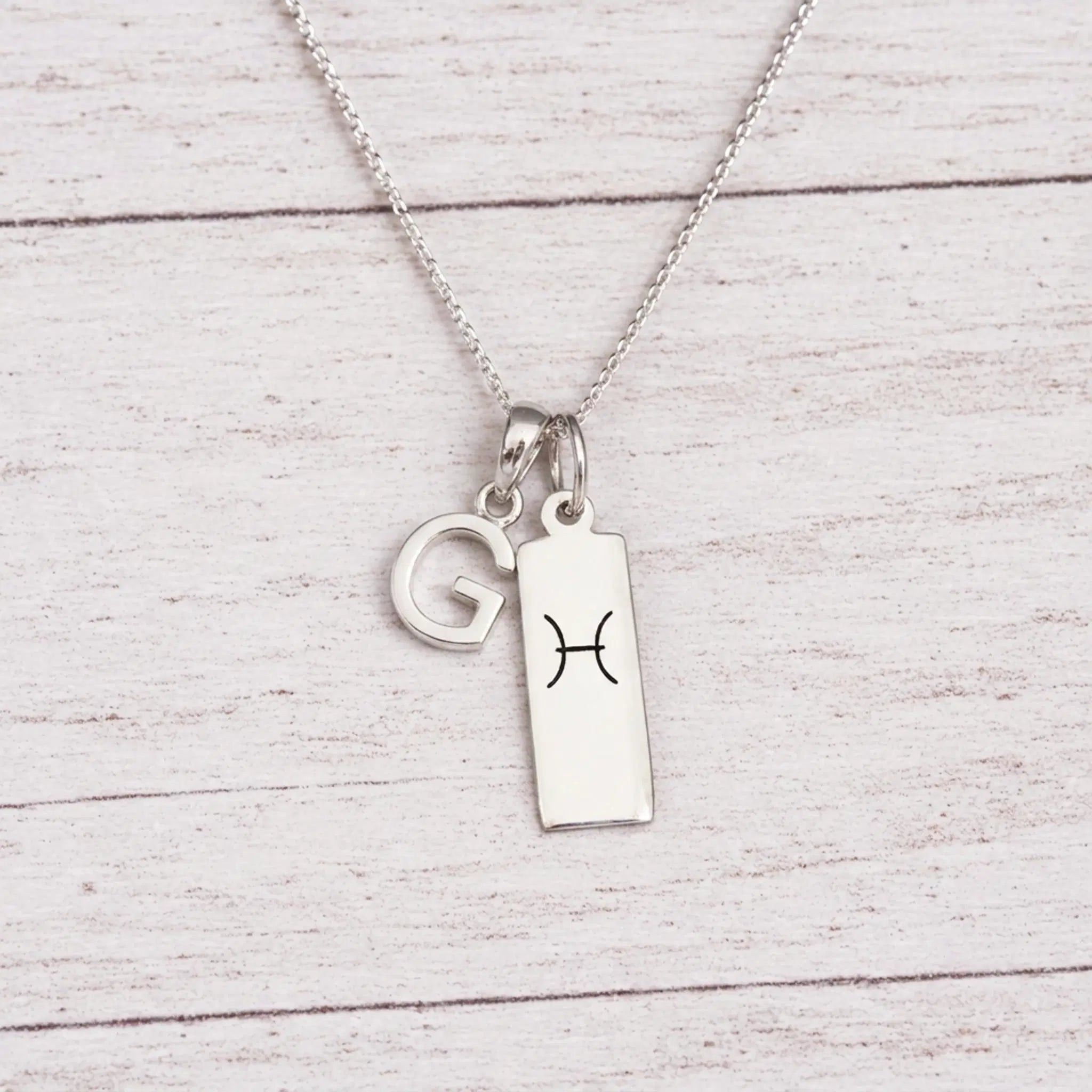 sterling silver G initial Pisces Necklace on a fine silver chain against a light wooden background