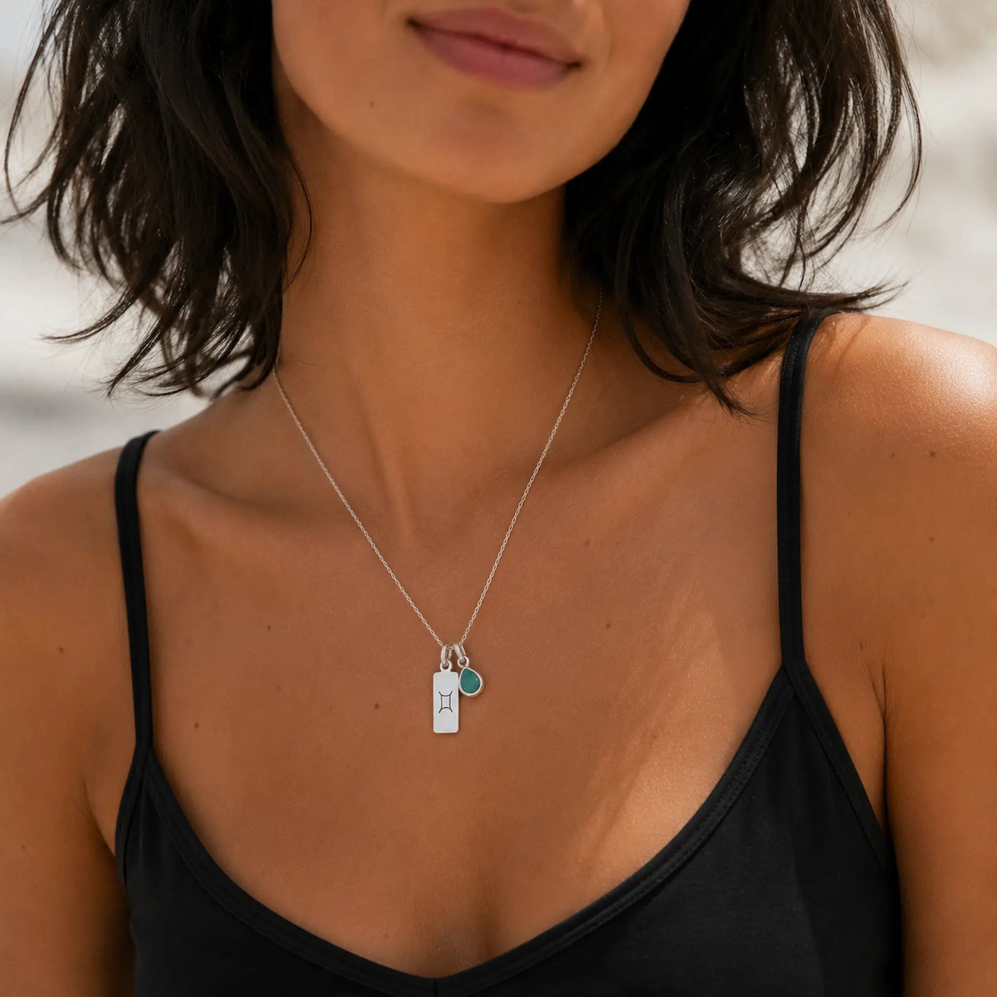 sterling silver gemini line glyph pendant and teardrop may birthstone natural emerald pendant necklace on a person wearing a singlet.