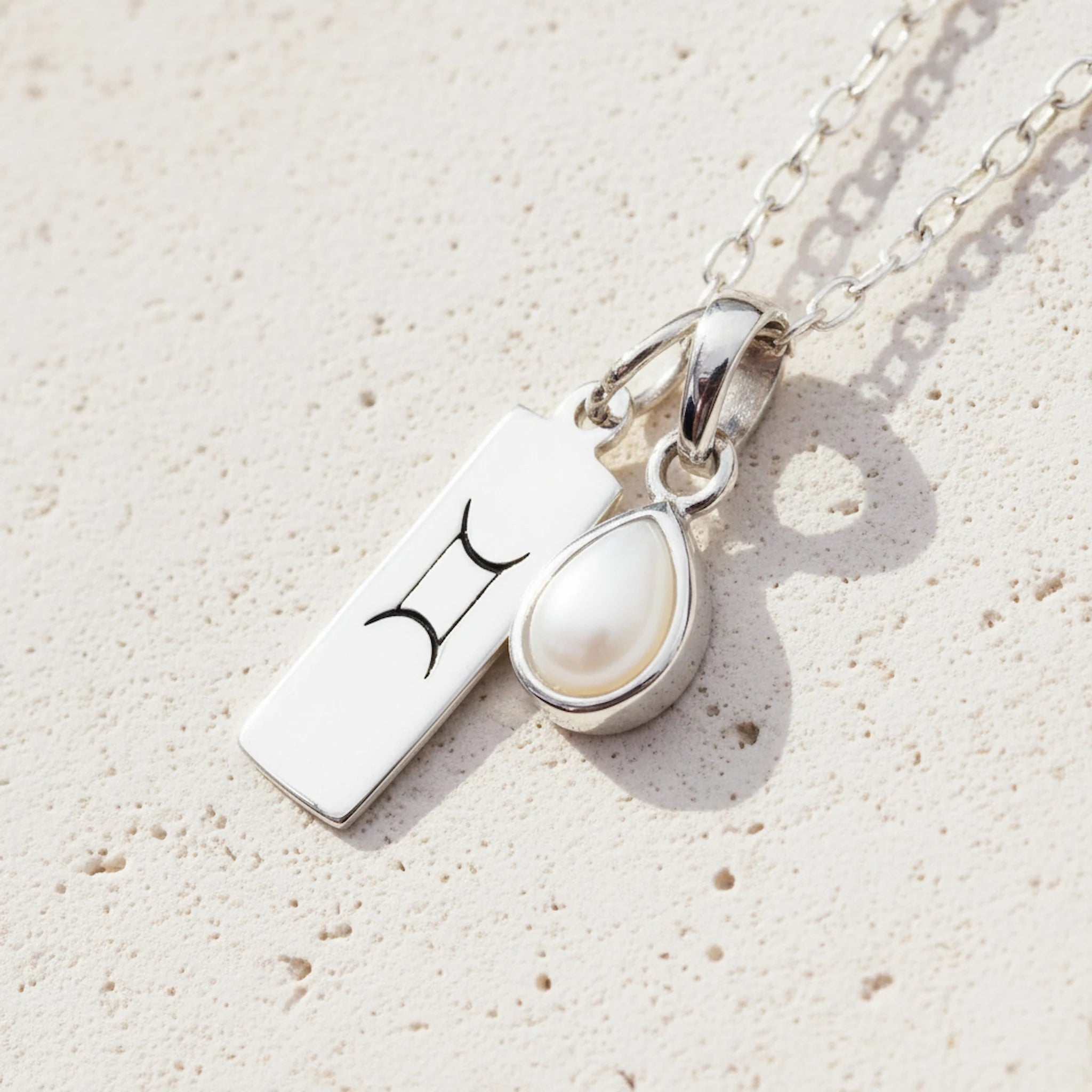 Sterling Silver necklace with a tear drop june birthstone pear pendant with a gemini zodiac pendant on a light background