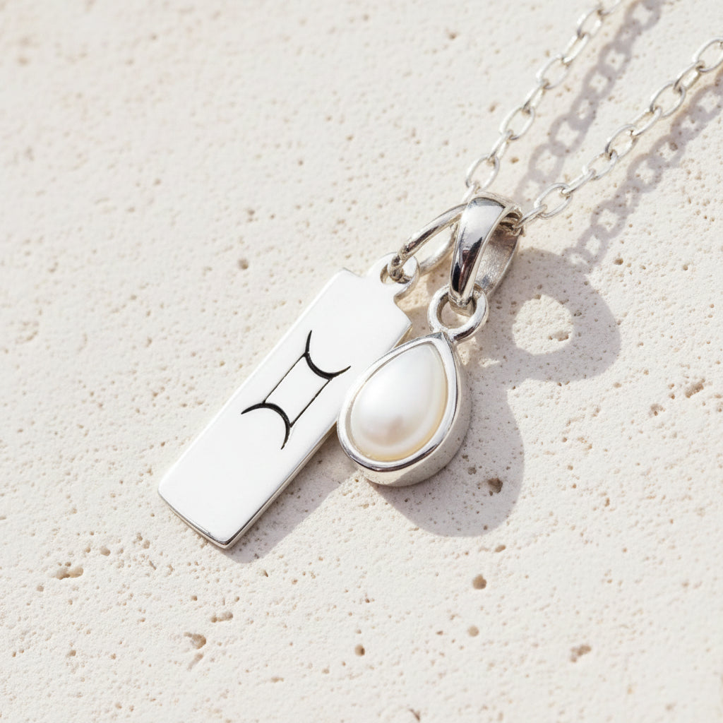 sterling silver chain with a Gemini zodiac pendant and tear drop  pearl pendant on a organic surface