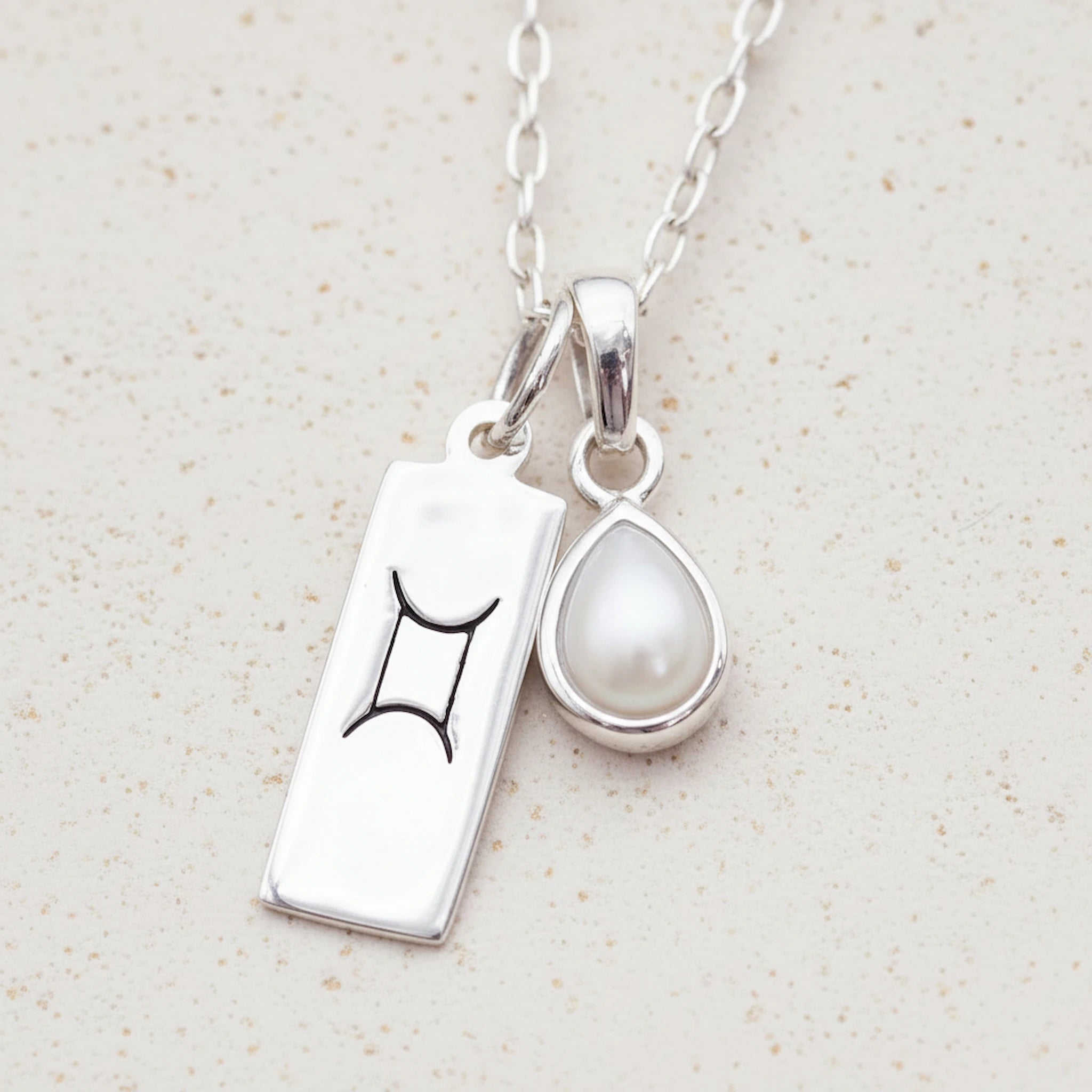 Sterling Silver necklace with a tear drop june birthstone pear pendant with a gemini zodiac pendant on a light background