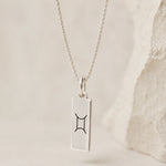 sterling silver fine chain necklace with a rectangle pendant engraved with the gemini zodiac line glyph symbol hanging.