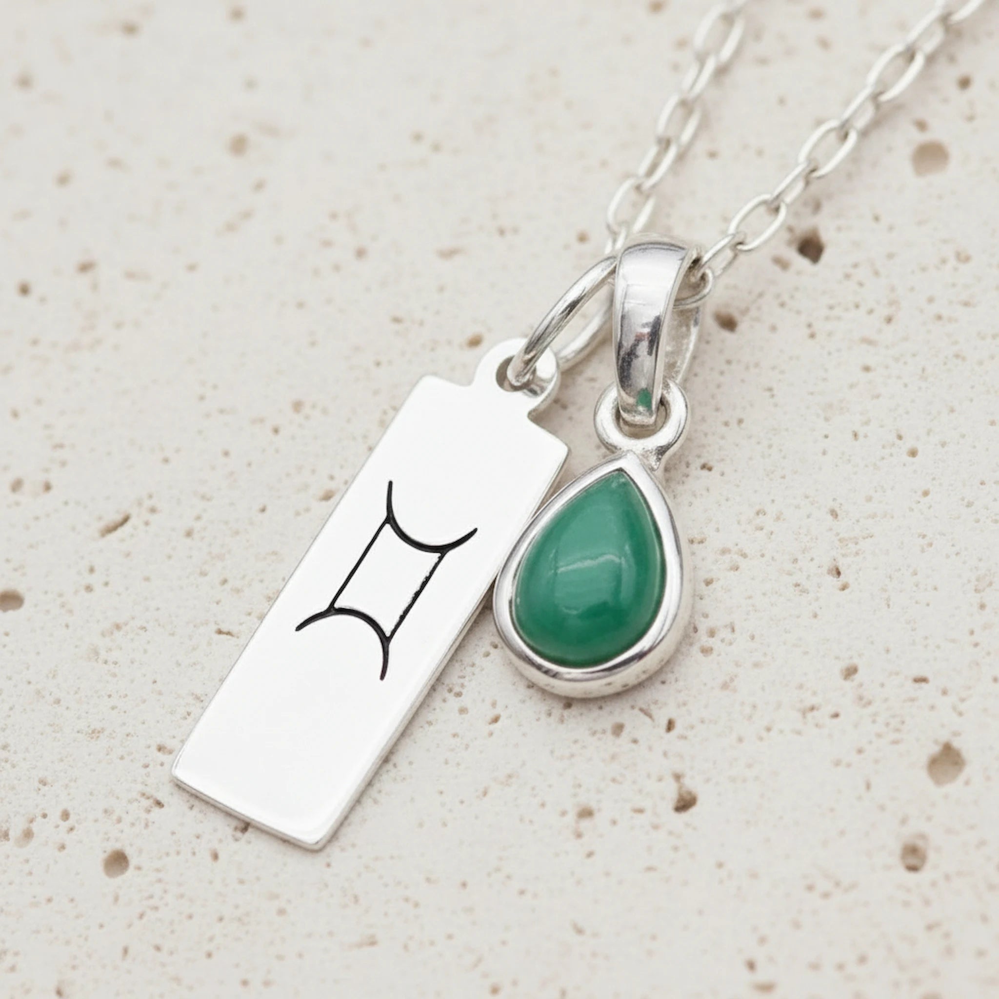 Sterling Silver necklace with a May Birthstone emerald gemstone pendant and a Gemini Zodiac pendant on a white background