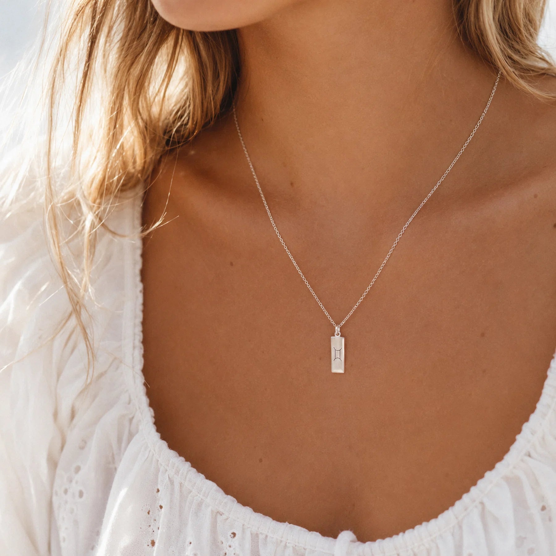 model wearing a dainty sterling silver fine chain necklace with a rectangle pendant with gemini zodiac line gylph engraving