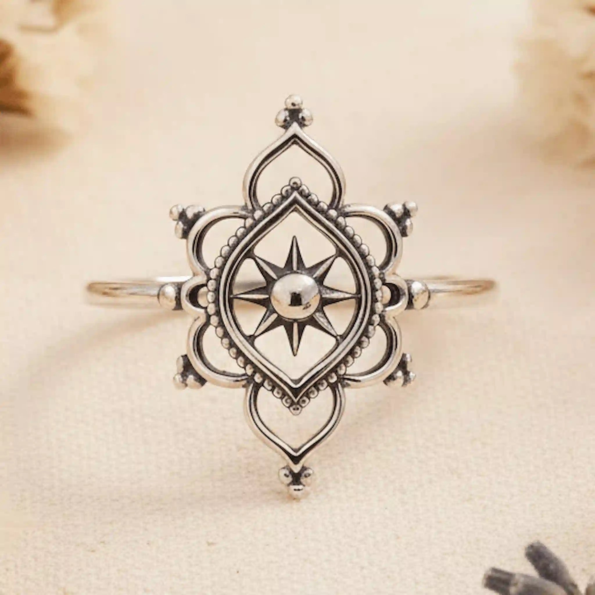 Silver ring with intricate design on a beige fabric background