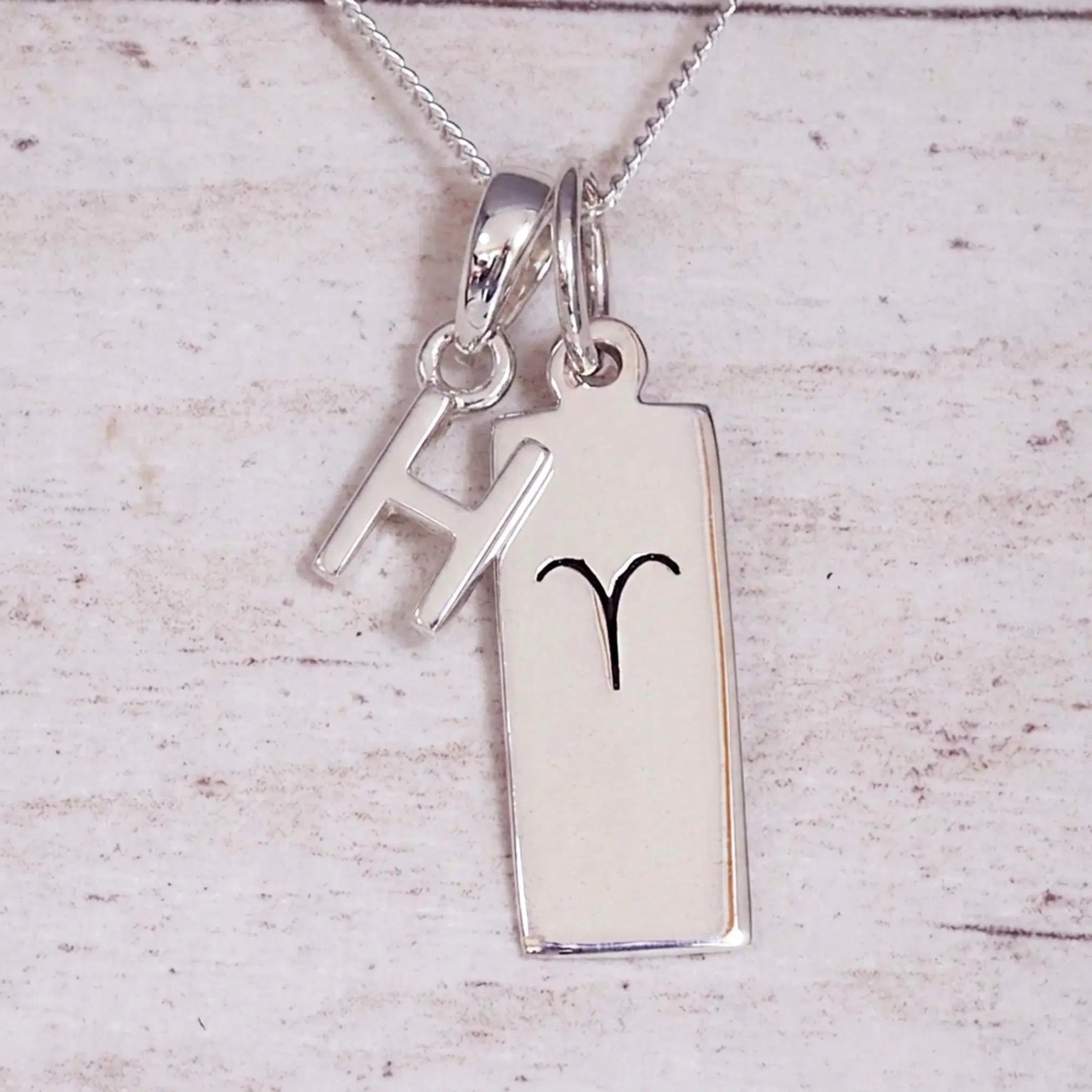 Sterling Silver H Initial pendant and Aries necklace on a fine silver chain on a light wooden background