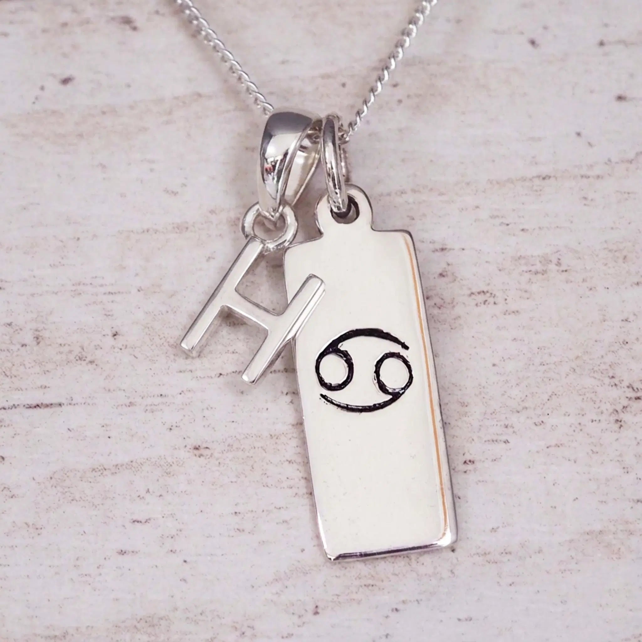 Sterling Silver H Initial Cancer Zodiac Star Sign Necklace on a fine silver chain against a light wooden background