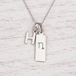 sterling silver initial H pendant and capricorn necklace on a fine silver chain against a light wooden background