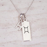 Sterling silver H initial and GeminI Necklace on a fine silver chain on a light wooden background