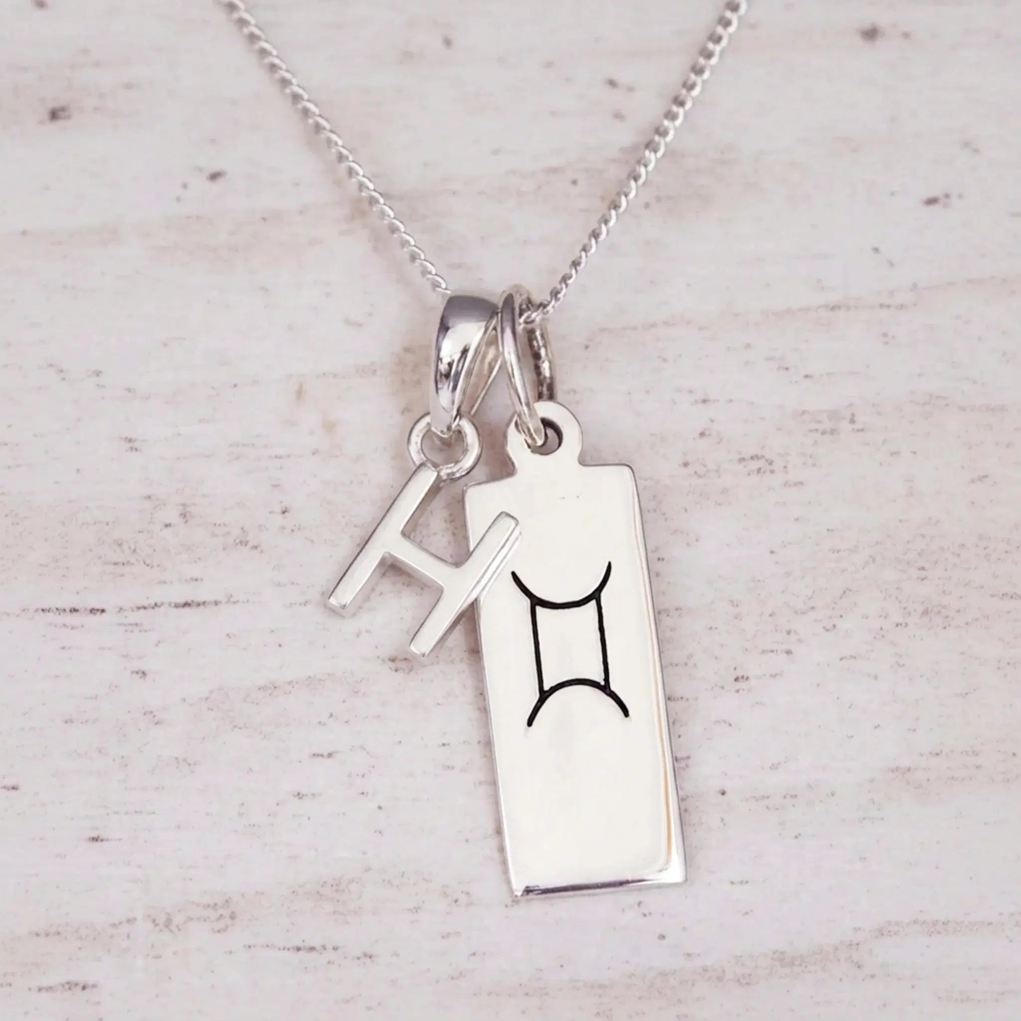 Sterling silver H initial and GeminI Necklace on a fine silver chain on a light wooden background