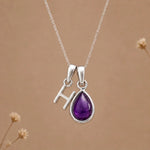 sterling silver initial v february birthstone natural amethyst pendant necklace against a dark warm beige background