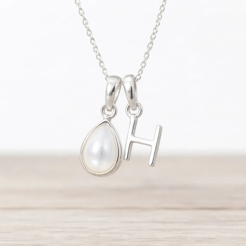 Silver necklace with a teardrop-shaped pearl pendant and 'H' initial on a light background