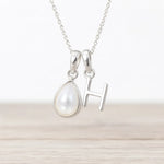 Silver necklace with a teardrop-shaped pearl pendant and 'H' initial on a light background