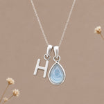 Sterling silver initial H and November natural blue topaz necklace on a taupe background with sparse ivory flowers
