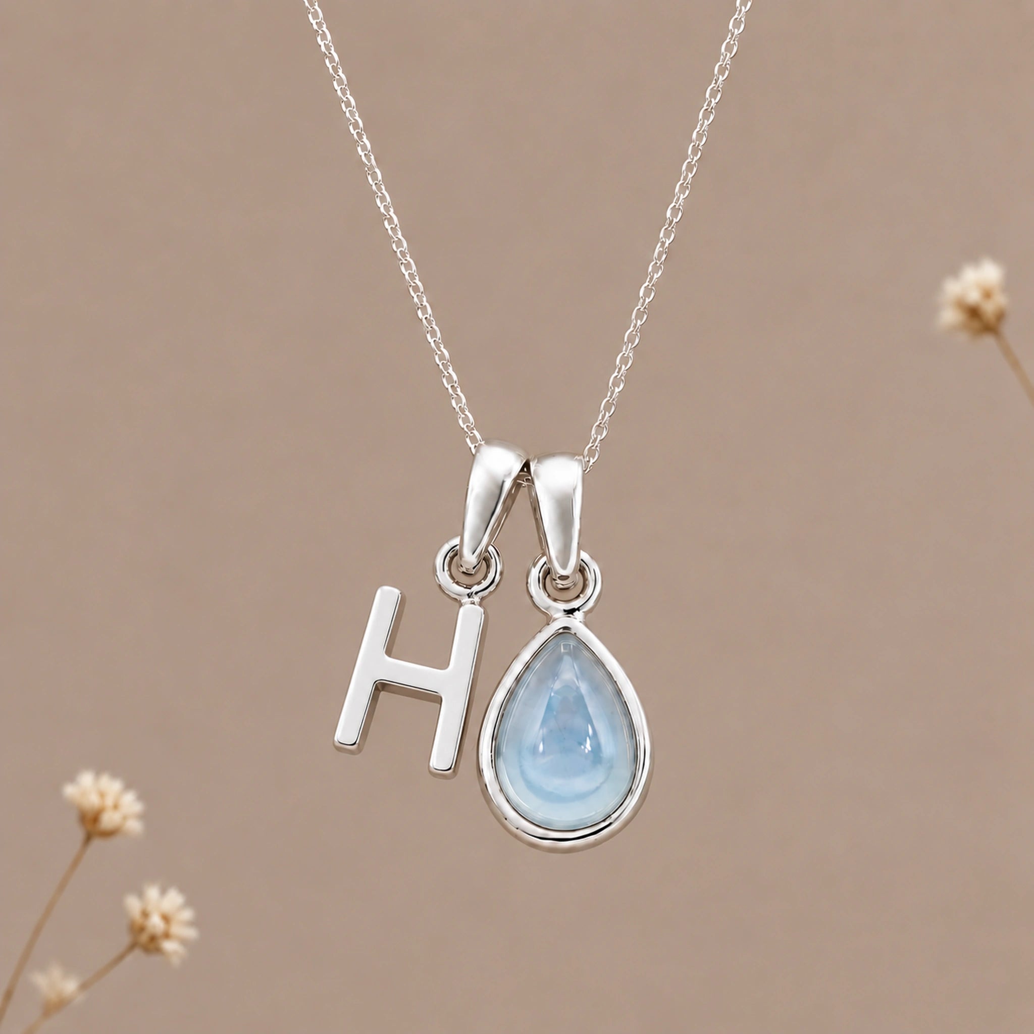 Sterling silver initial H and November natural blue topaz necklace on a taupe background with sparse ivory flowers