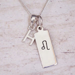 Sterling silver Leo initial necklace with a letter H and engraved zodiac bar on wood