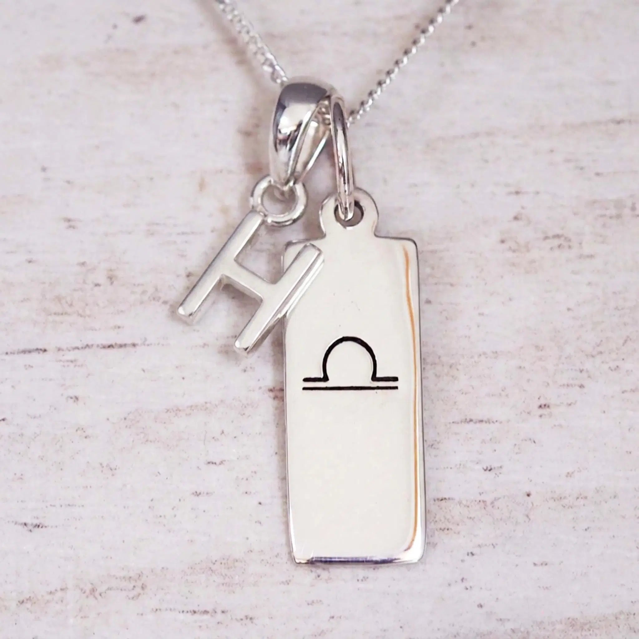 sterling silver initial h libra zodiac star sign pendant necklace against a light wooden background