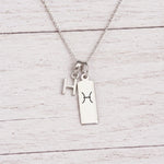 sterling silver H initial Pisces Necklace on a fine silver chain against a light wooden background