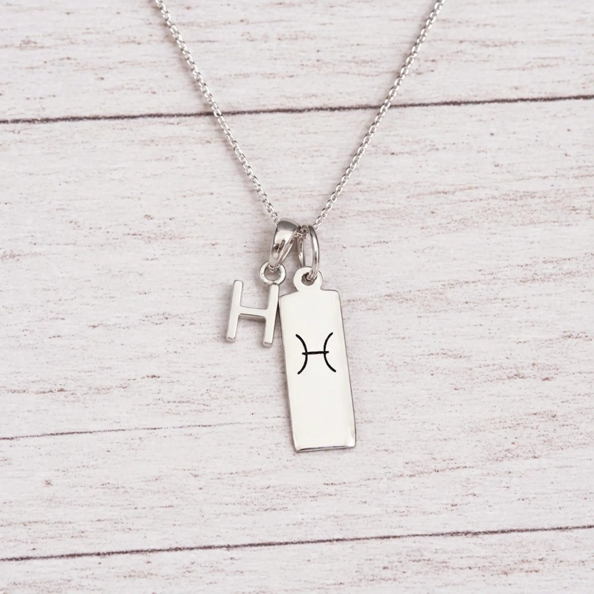 sterling silver H initial Pisces Necklace on a fine silver chain against a light wooden background
