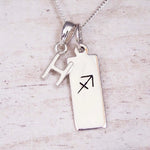 sterling silver initial h sagittarius zodiac star sign pendant necklace against a light wooden background