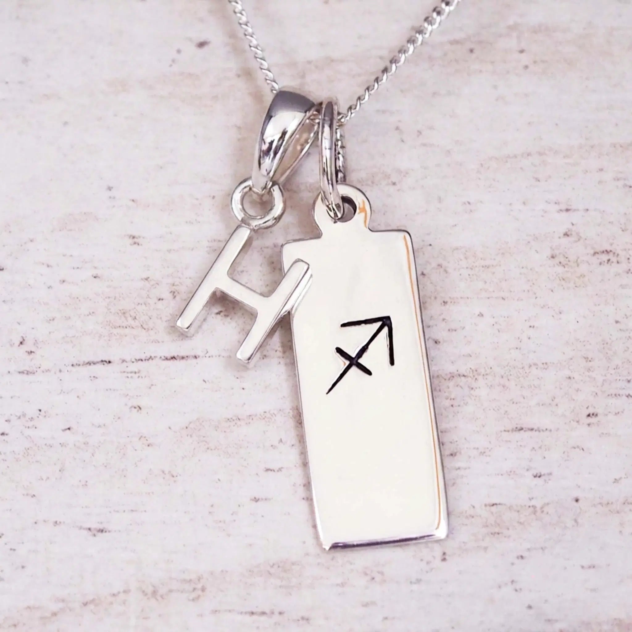 sterling silver initial h sagittarius zodiac star sign pendant necklace against a light wooden background