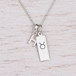 Sterling silver H initial Pendant and Taurus Necklace on a fine silver chain on a light wooden background