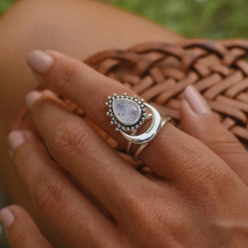 Silver moonstone ring with a moonstone gemstone on a person's finger against a blurred natural background 