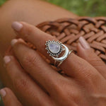 Silver moonstone ring with a moonstone gemstone on a person's finger against a blurred natural background 