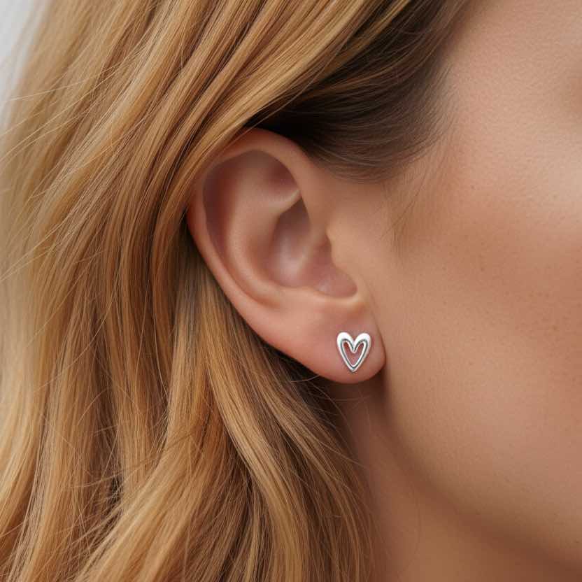 Close-up of an ear wearing a heart-shaped earring with blonde hair.