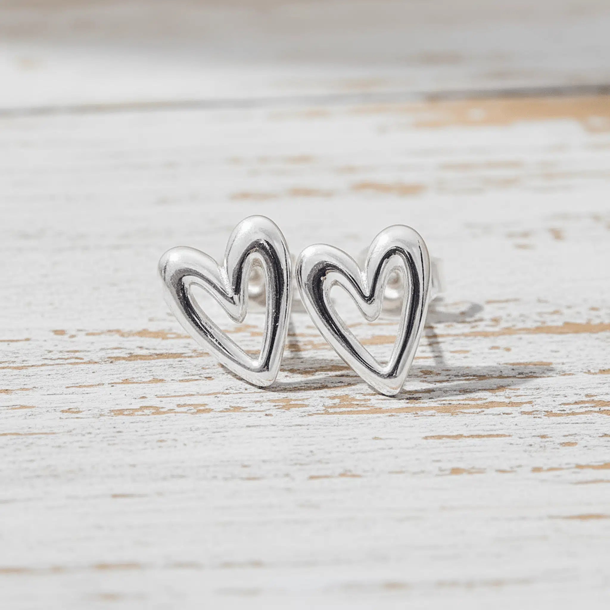 Silver heart-shaped earrings on a light wooden surface